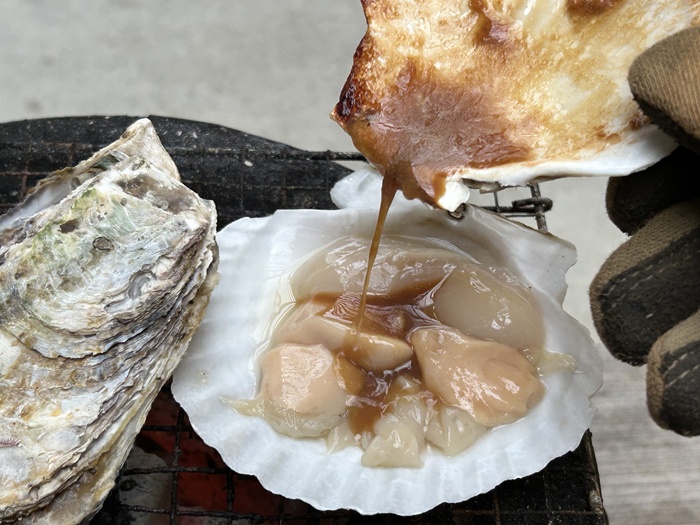 先に焼いたホタテ貝に残った醤油バター汁を次に焼くホタテ貝に移している光景